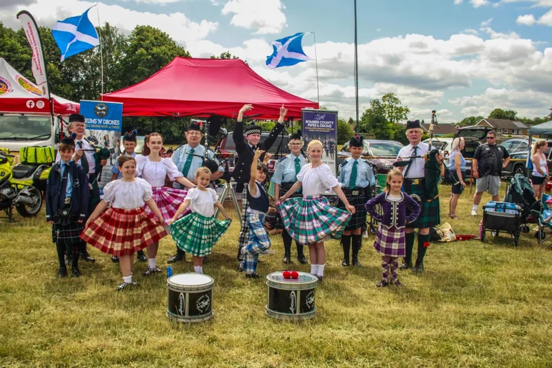 Young Highland dancers and band members with drums in front of a red gazebo at Langtoft Festival