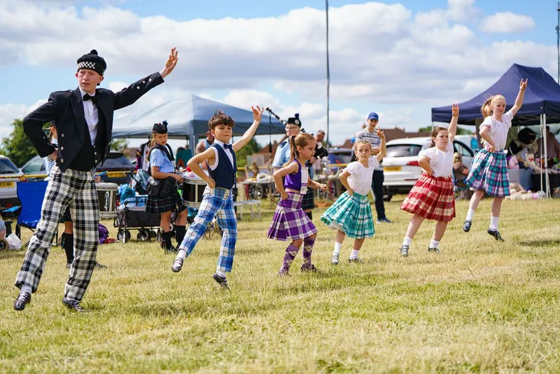 Young Highland dancers in tartan skirts leaping on a showground field